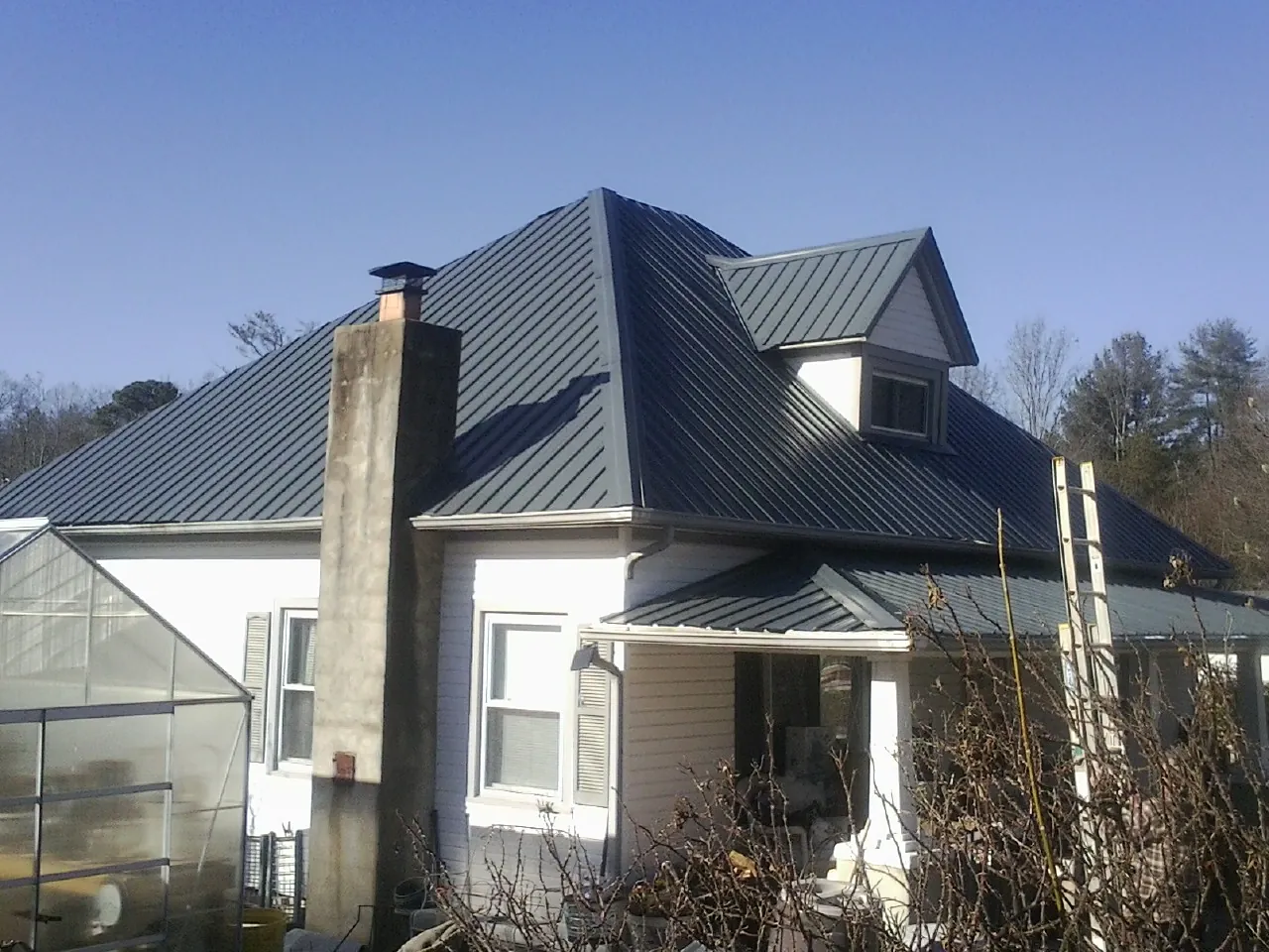 Dark blue standing seam metal roof on a white farmhouse with dormer — Slate & Tile Roof Repair by Roofing Brothers in Appling