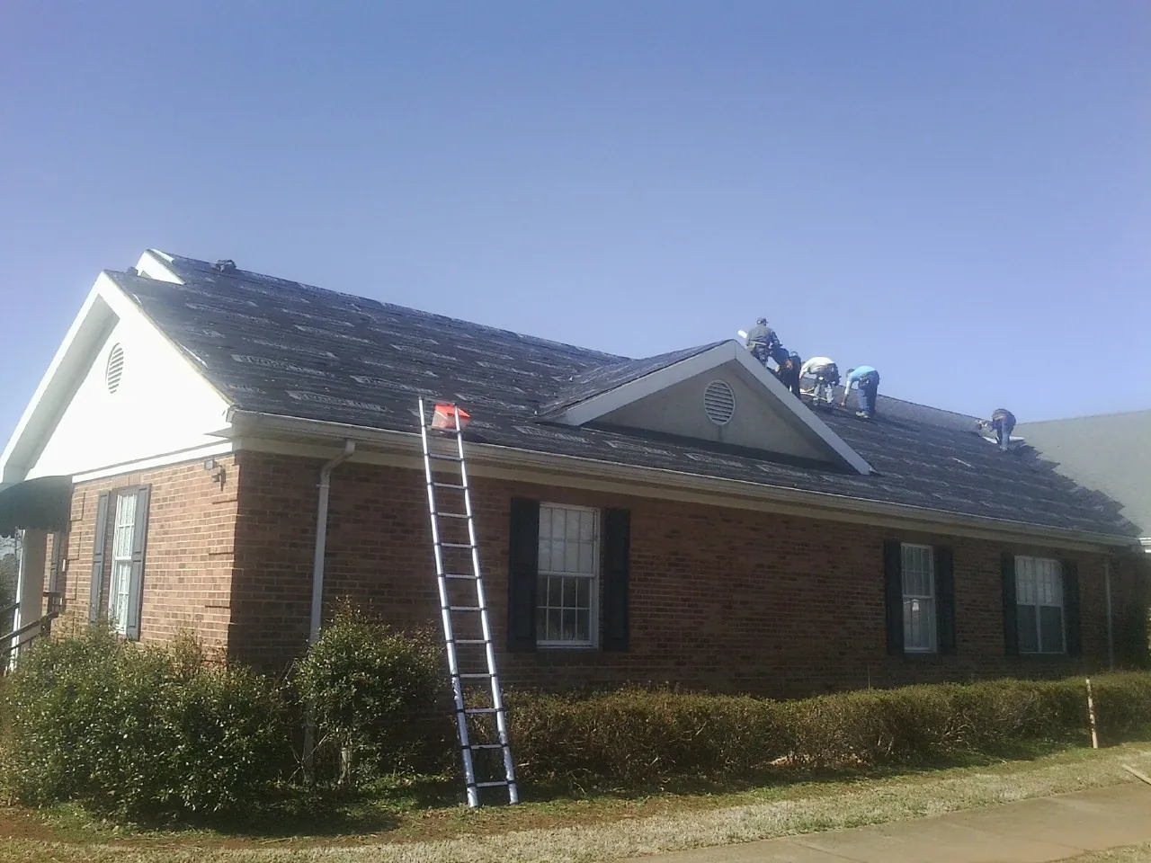 Crew tearing shingles off a brick ranch roof with a ladder set — Emergency Roof Repair work by our crew in Appling