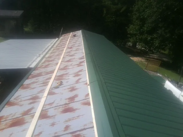 Old rusted panels beside newly installed green metal roofing — Wind Damage Roof Repair by Roofing Brothers in Appling