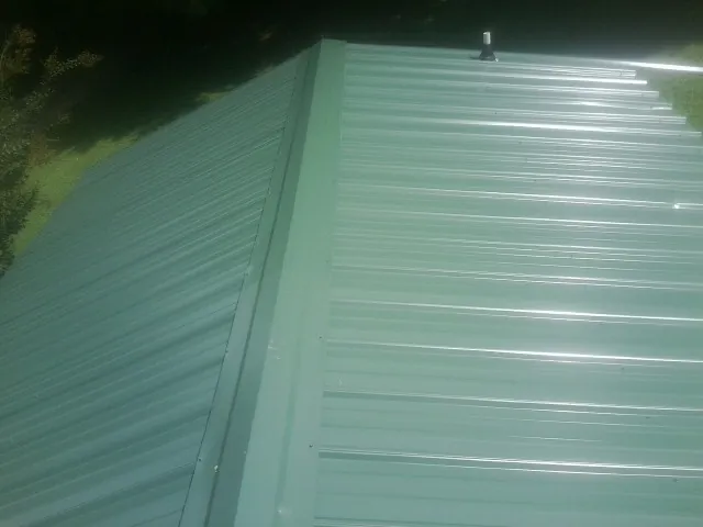 New green metal panels meeting at the ridge of a roof — Flat Roof Repair work by our crew in Appling